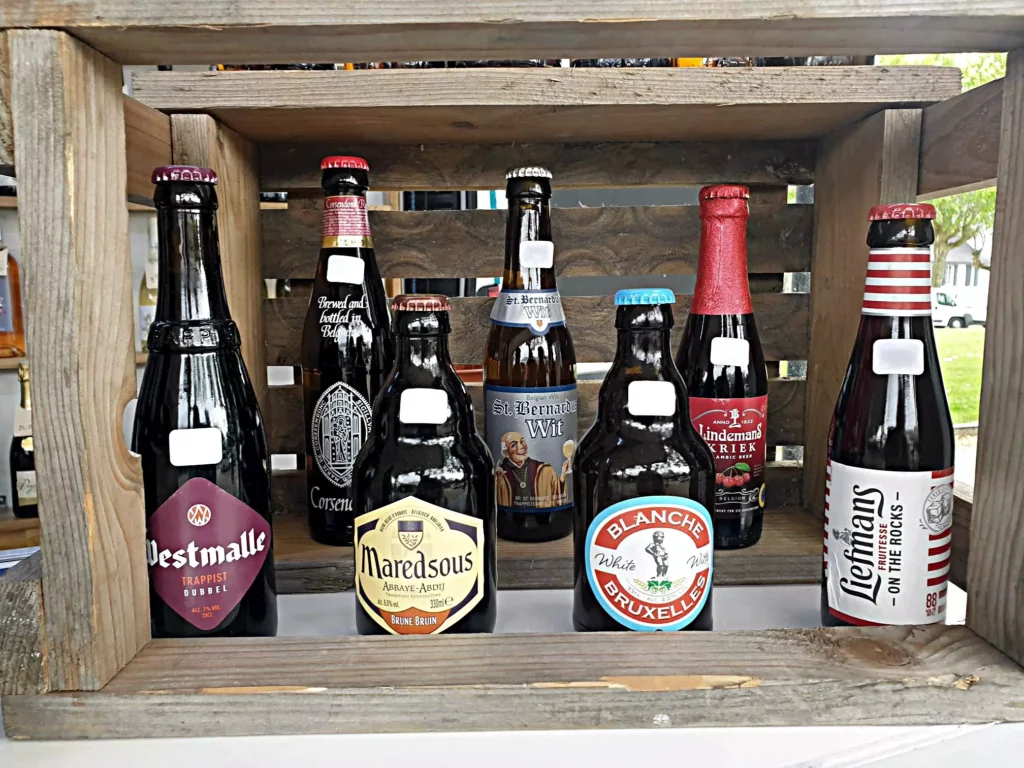 Assortiment varié de douze bières belges artisanales comprenant des bières blondes, blanches, ambrées, brunes et fruitées dans une présentation élégante
